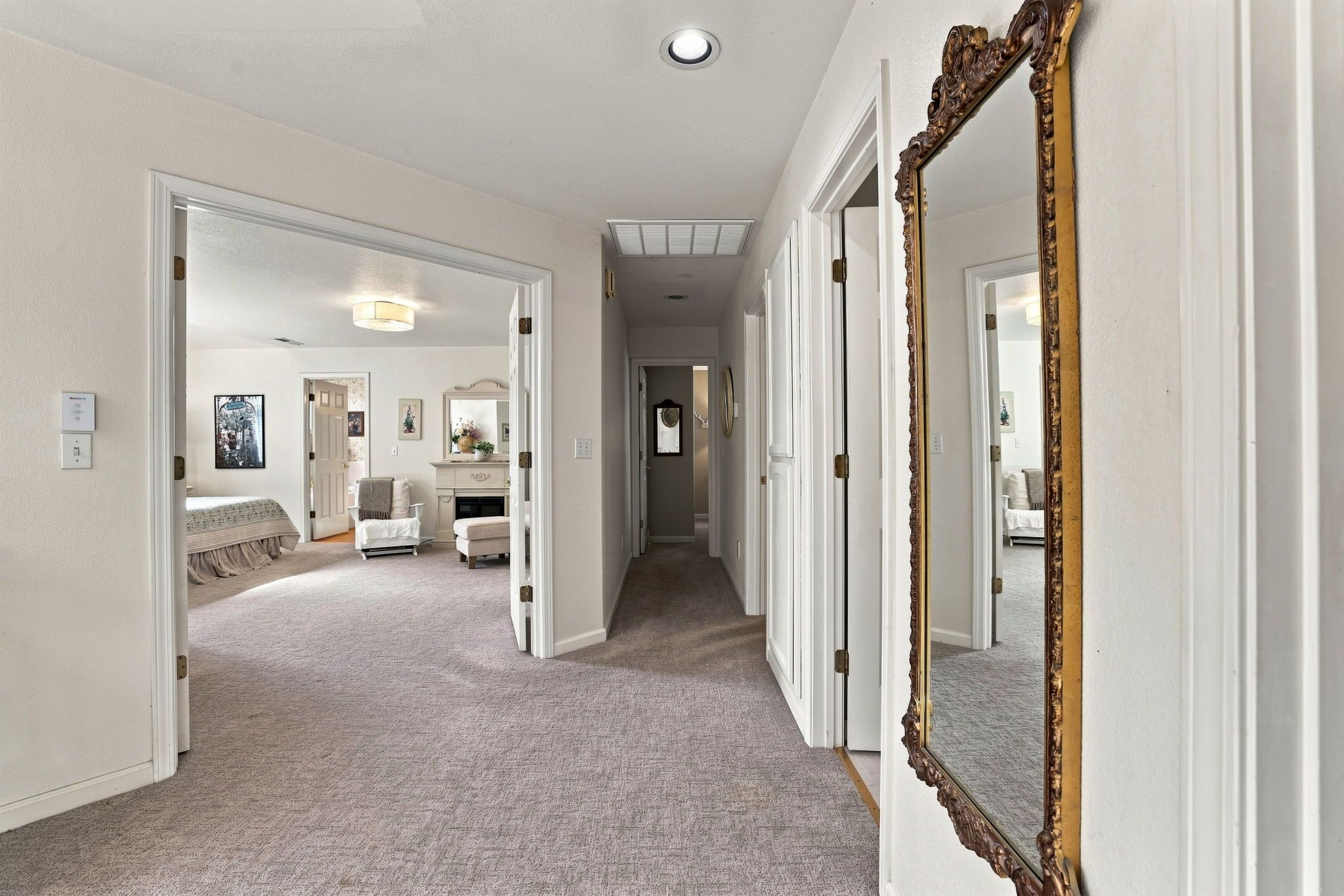 A hallway with a carpeted floor, white walls, and a large mirror with an ornate frame.