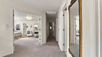 A hallway with a carpeted floor, white walls, and a large mirror with an ornate frame.