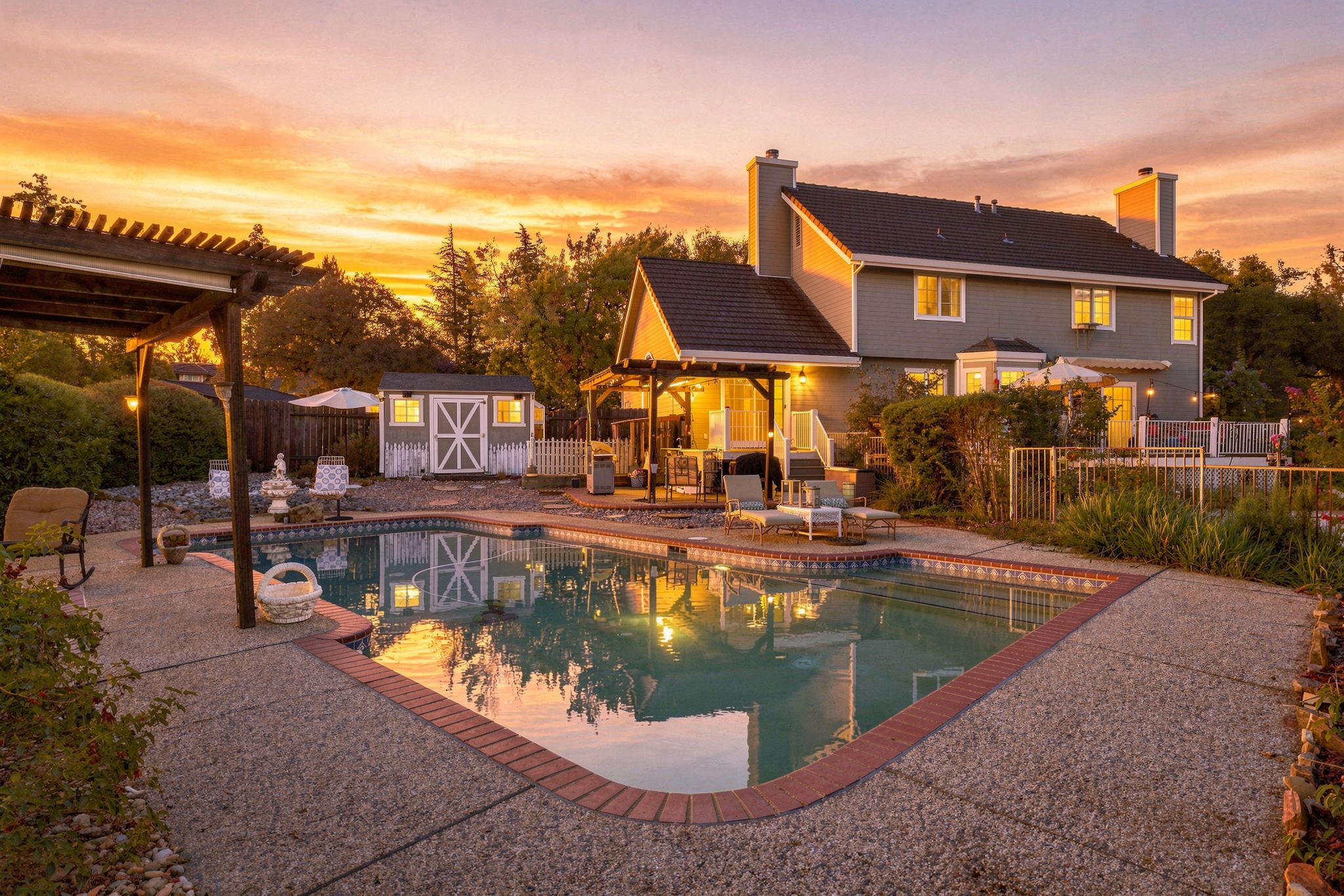 A residential property with a swimming pool, a covered patio, and a house with a fenced yard.