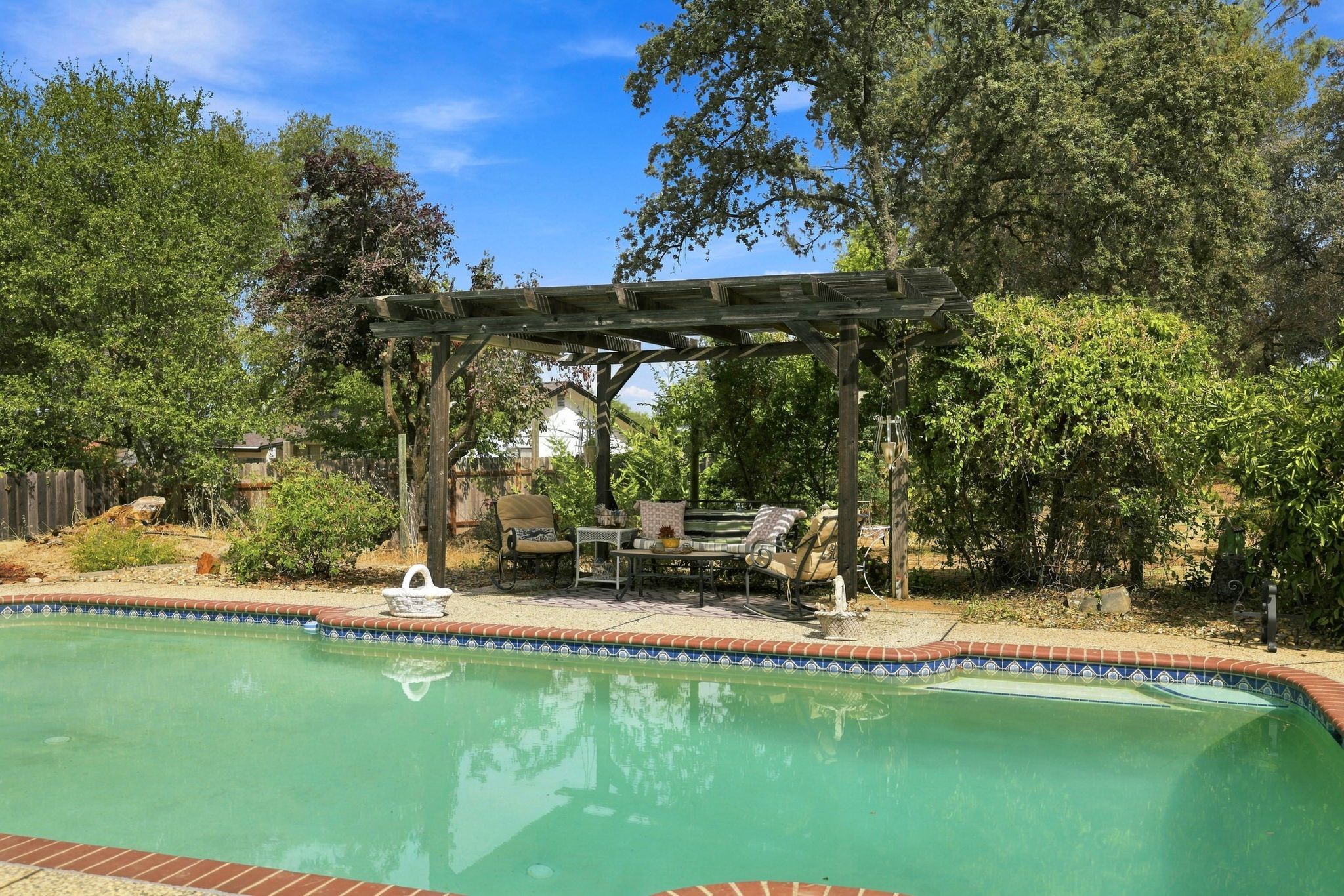 A swimming pool with a wooden pergola and outdoor furniture.
