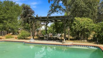 A swimming pool with a wooden pergola and outdoor furniture.