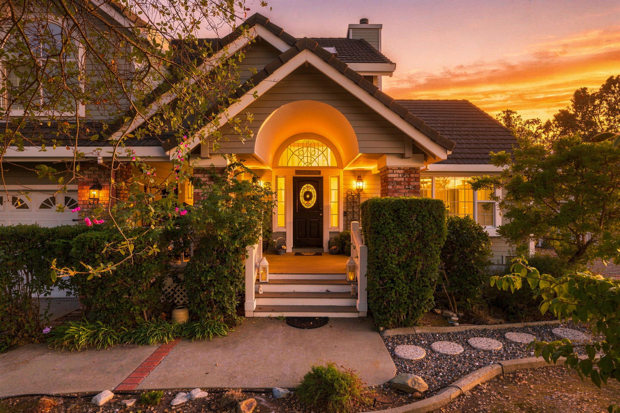 A two-story house with a front porch, a brick chimney, and a well-lit entrance.