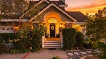A two-story house with a front porch, a brick chimney, and a well-lit entrance.
