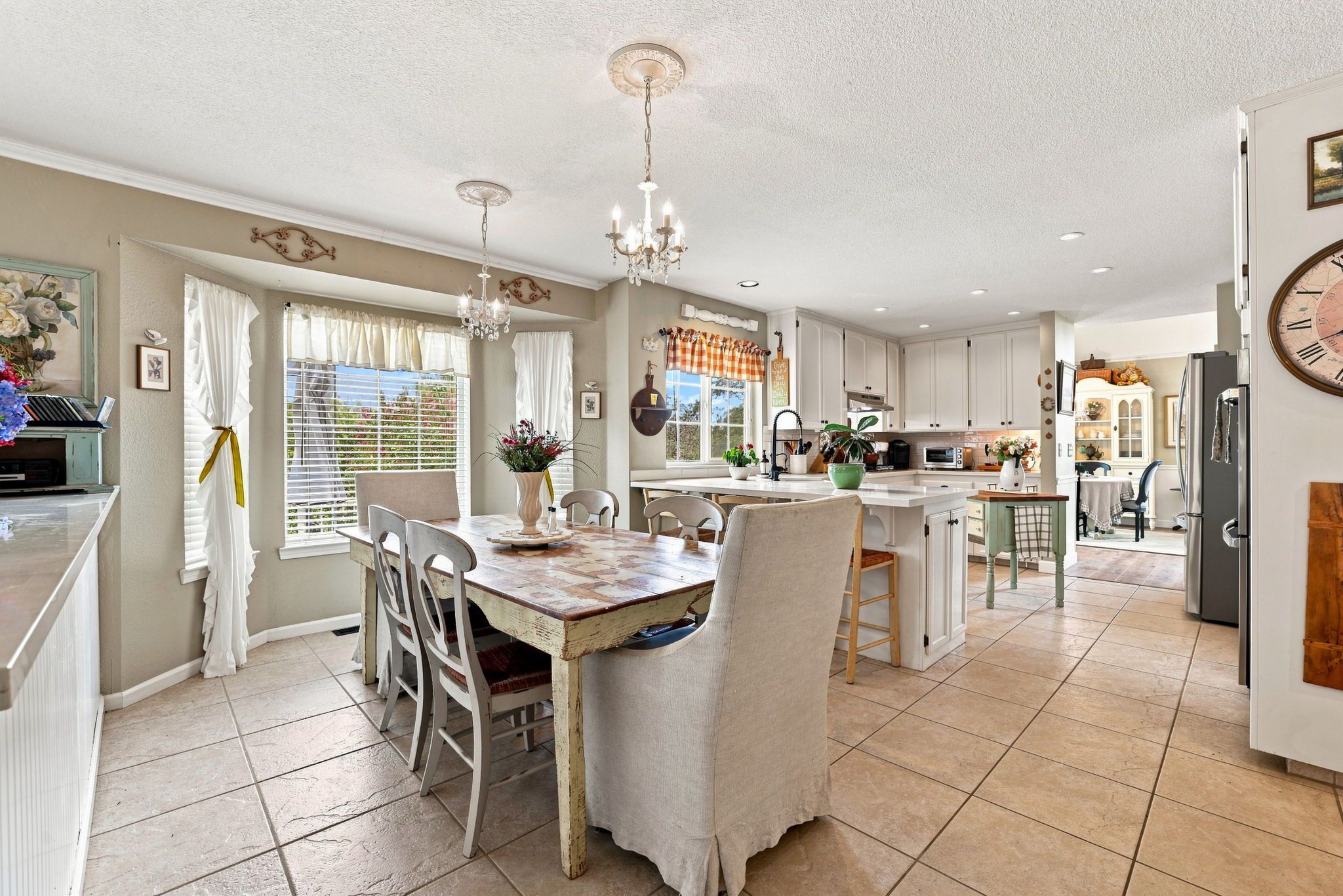 A spacious kitchen with white cabinetry, a dining area with a wooden table and chairs, and a large clock on the wall.