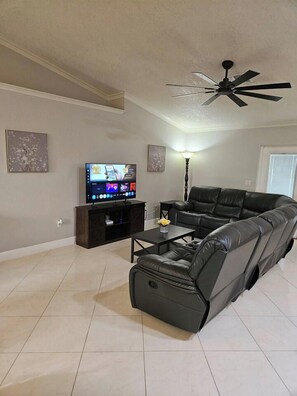 A living room with a sectional sofa, a flat-screen TV, a ceiling fan, and a lamp. - 3 Bedroom Cul-de-Sac Pool Home (Lakeland)