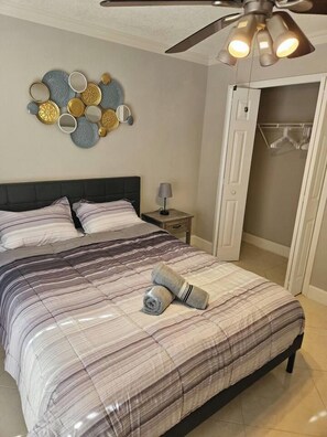 Une chambre à coucher comprenant un lit, une table de chevet, un ventilateur de plafond et un miroir fixé au mur.