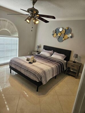 A bedroom with a bed, a ceiling fan, a wall decoration, and a nightstand. - 3 Bedroom Cul-de-Sac Pool Home (Lakeland)