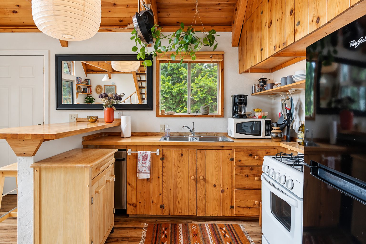A kitchen with wooden cabinets, a microwave, a stove, and a window with a view of greenery.