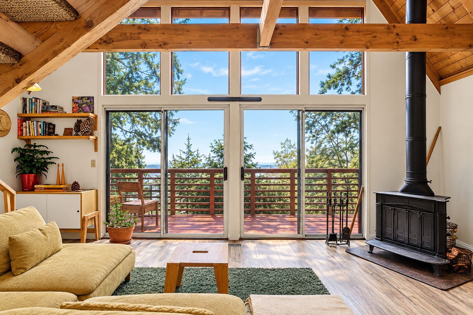 A cozy living room with a sofa, a fireplace, a bookshelf, and a view through large glass doors to an outdoor deck.