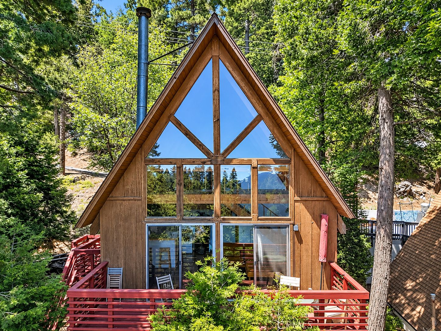 A wooden cabin with a triangular roof, large windows, and a red deck.