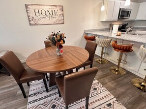 A dining area with a round wooden table, six brown chairs, a vase with flowers, and a patterned rug. - Sage and Stillness Extended Stay Retreat (Killeen)