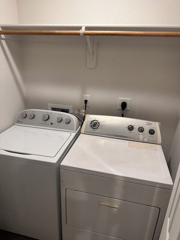 Una sala de bugaderia amb dues piles de rentadores i assecadores, una prestatgeria de fusta per a estendre la roba i una paret blanca.