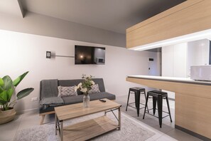 A modern living room with a sofa, coffee table, and a flat-screen TV mounted on the wall. - Quiet Studio · Select Design (H18)   (Providencia)