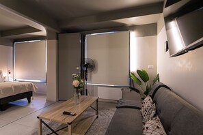 A modern bedroom with a bed, a sofa, a coffee table, and a TV mounted on the wall. - Quiet Studio · Selected Design (H18) (Providencia)