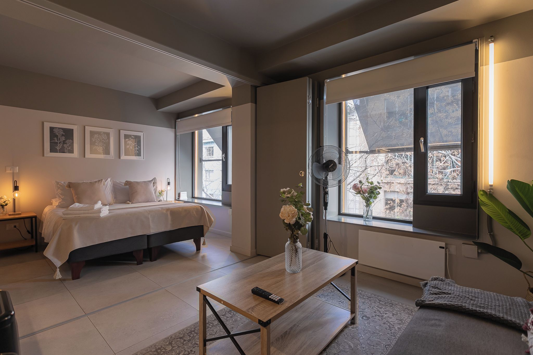 A bedroom with a bed, bedside table, and a window with a view of buildings.