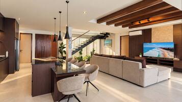 A modern living room with a glass dining table, sofas, and a large flat-screen TV.