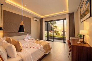 A hotel room with a bed, bedside table, lamp, and a view of the outdoors. - 3-Bedroom Beach Front Villa with Ocean View in Tulamben Karangasem Bali (Karangasem)