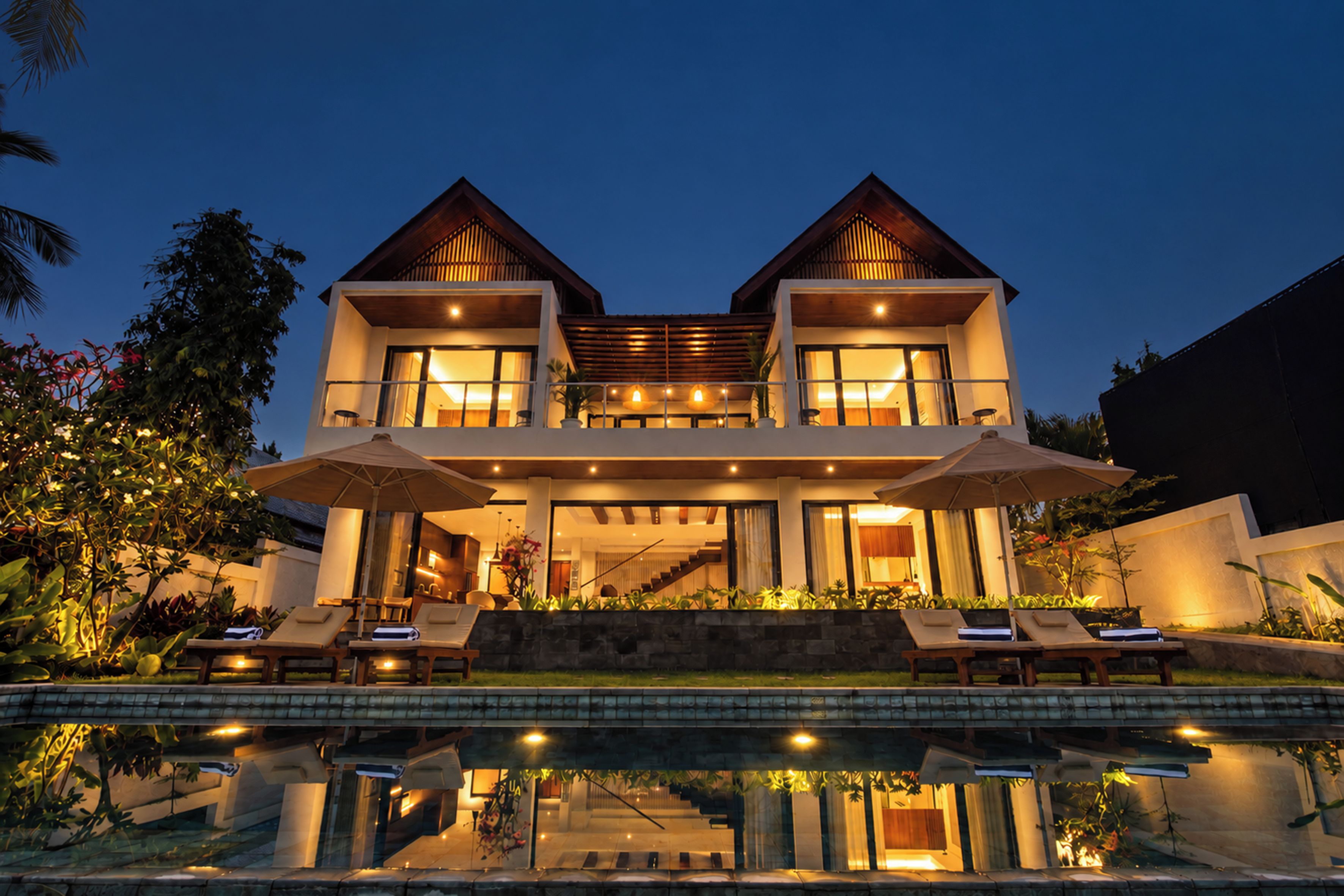 A two-story house with a swimming pool in front, featuring a modern design with large windows and a covered outdoor area.