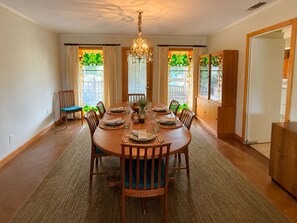 A dining room with a round table set for six, surrounded by chairs, a chandelier, and large windows with curtains. - Bluebird Habitat: A Marfa Home Away from Home (Marfa)