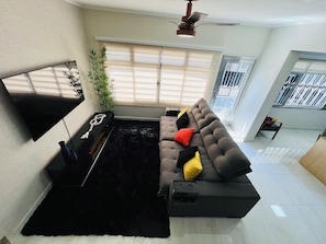 A modern living room with a flat-screen TV, a black sofa with colorful cushions, a black rug, and a ceiling fan. - Luxury Townhouse (São Paulo)