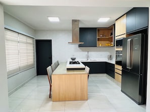 A modern kitchen with a central island, black appliances, and a tiled floor. - Luxury Townhouse (São Paulo)