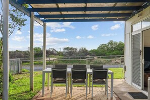 An outdoor patio with a table and chairs, a covered area, and a view of the surrounding landscape. - Beach Shack Escape Beach Just Across the Road (Aldinga Beach)