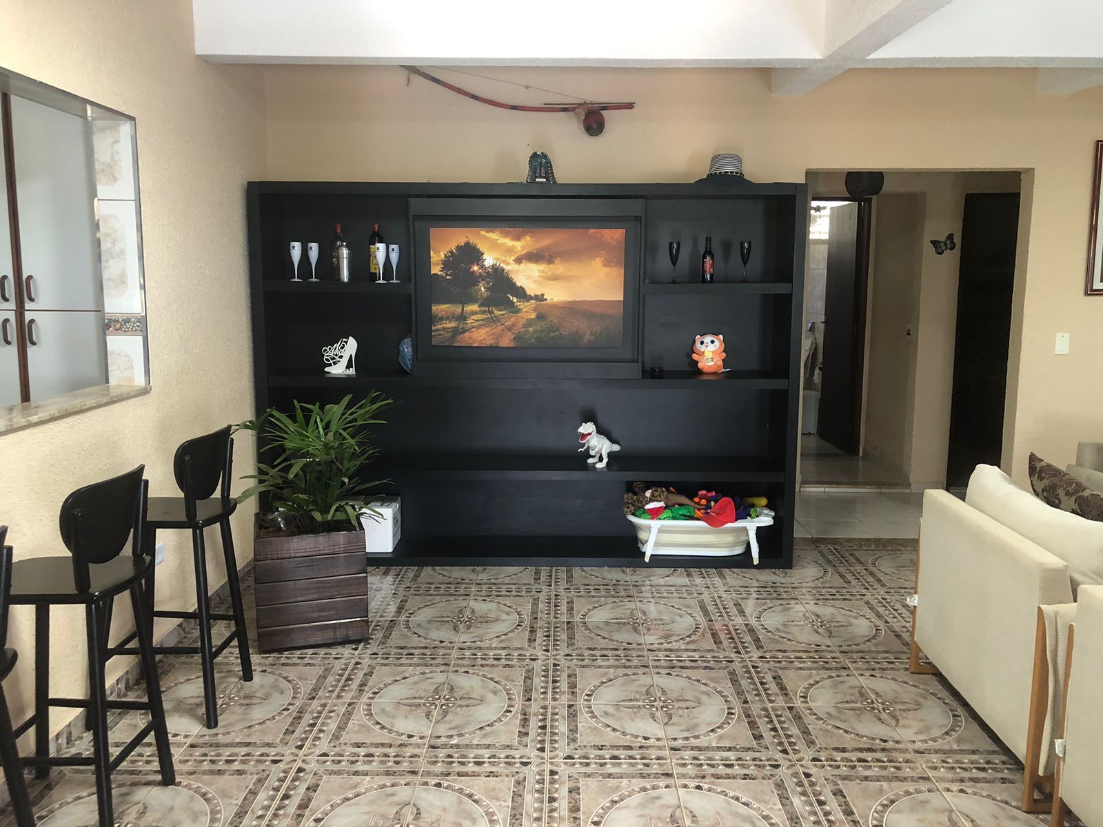 A living room with a black entertainment unit, a dining area with chairs and a table, and a patterned floor.
