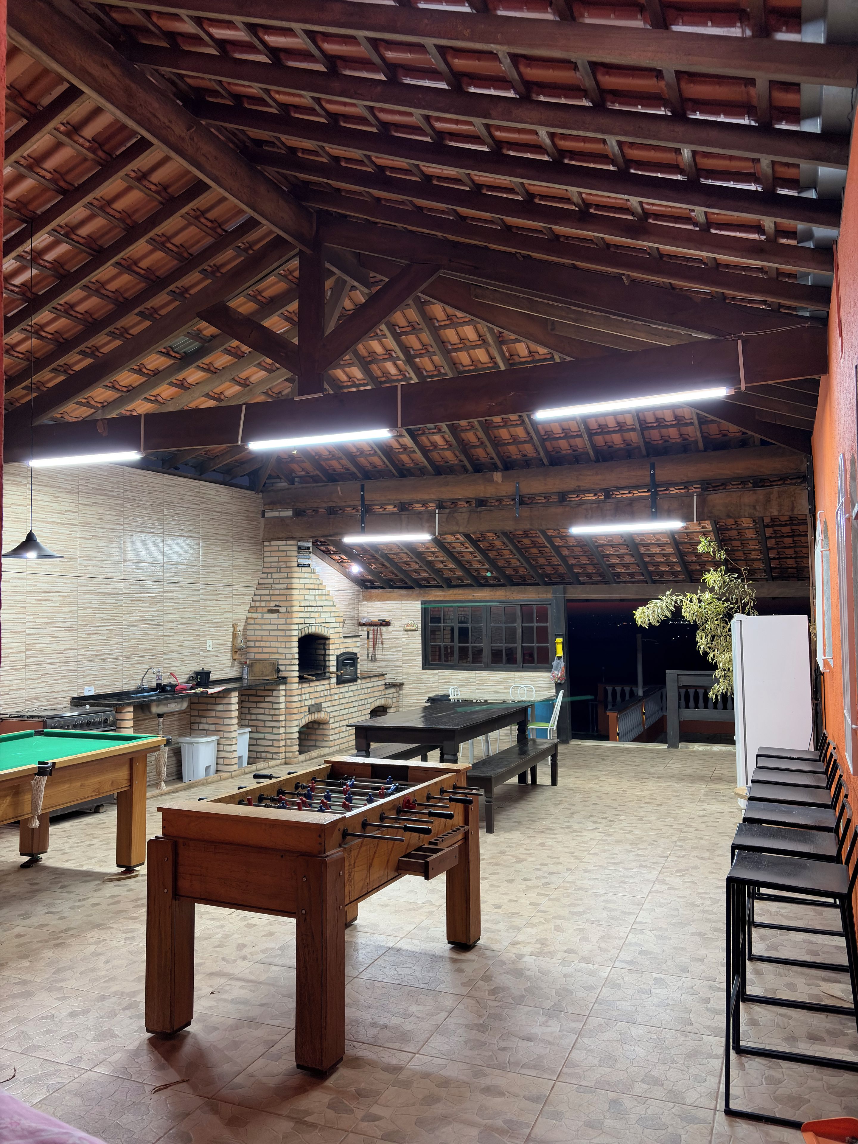 Un grand espace intérieur comprenant une table de billard, une table de baby-foot et un four à pizza en briques.