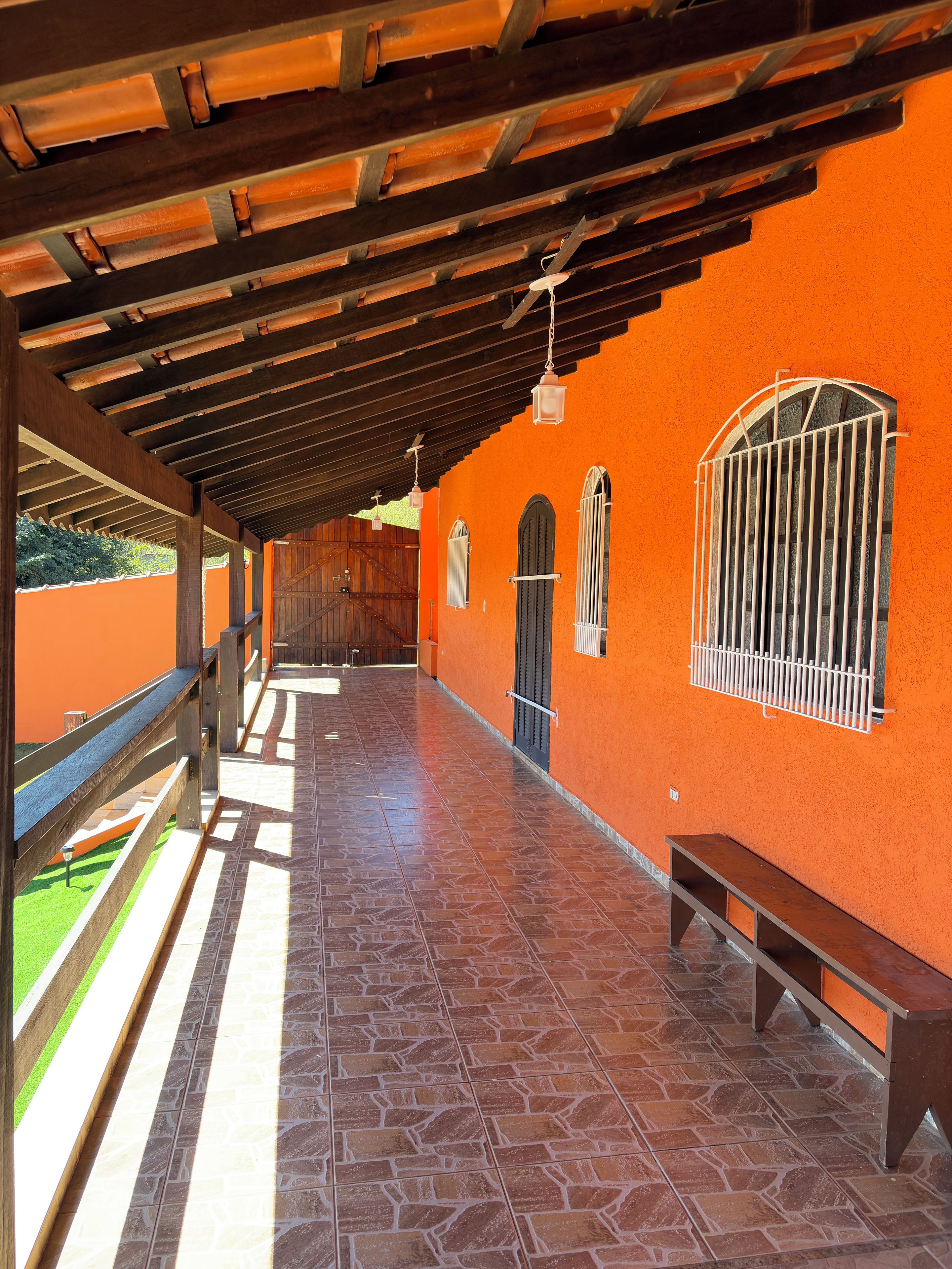 A covered outdoor area with a tiled floor, wooden benches, and a railing overlooking a green space.
