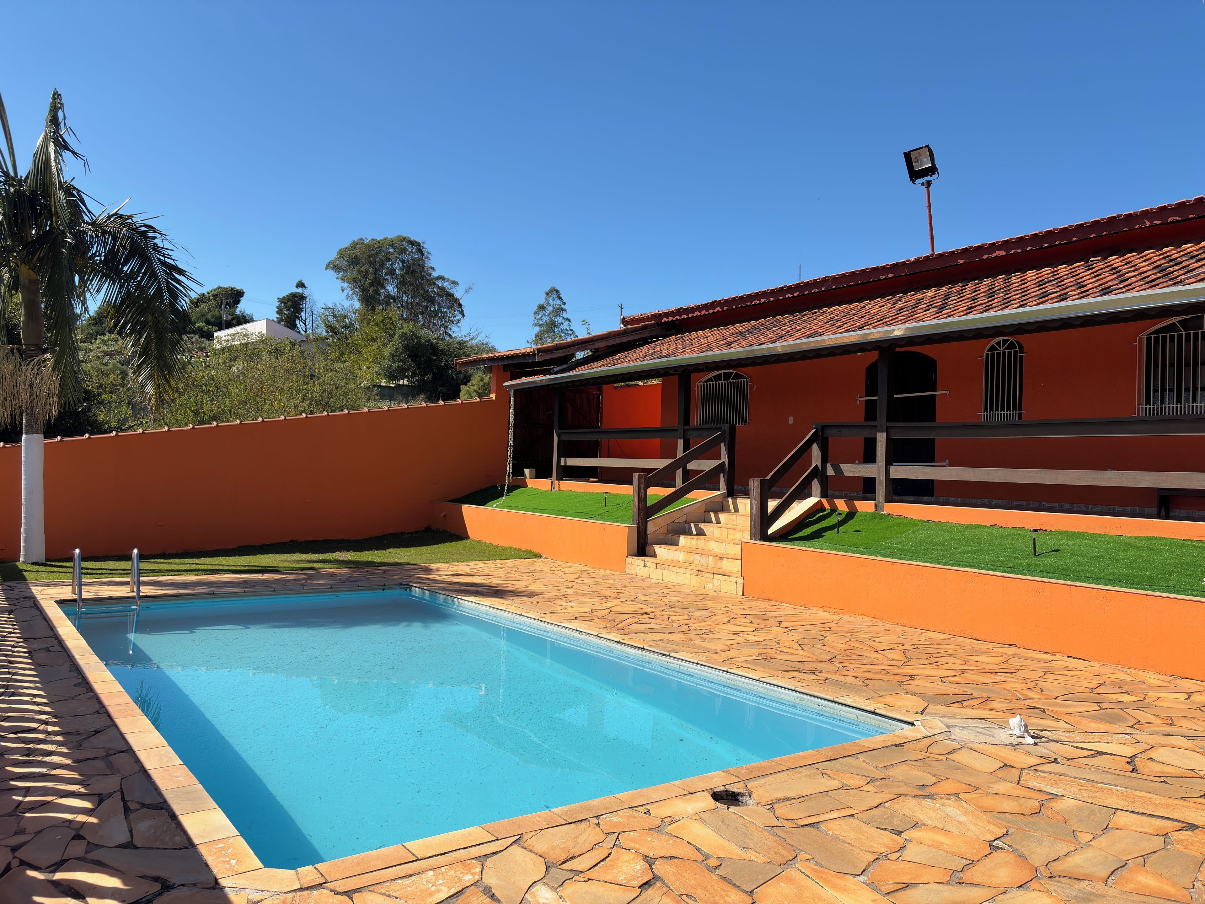 A swimming pool with a stone deck, a wooden staircase, and a building with a red-tiled roof.
