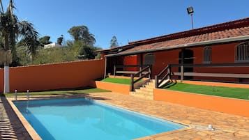 A swimming pool with a stone deck, a wooden staircase, and a building with a red-tiled roof.