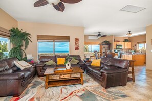 Ein Wohnzimmer mit einem großen Fenster, einer braunen Ledersofa-Garnitur, einem Couchtisch und Blick aufs Meer.