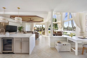 A spacious living area with a kitchen island, a dining area, and a large window offering a view of the outdoors. - NEW Mauna Lani Villa Sunset Designer Renovated (Waimea)
