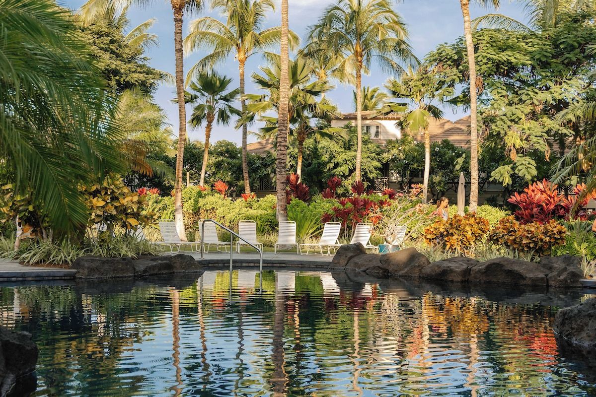 A pool area with lounge chairs and tropical vegetation.