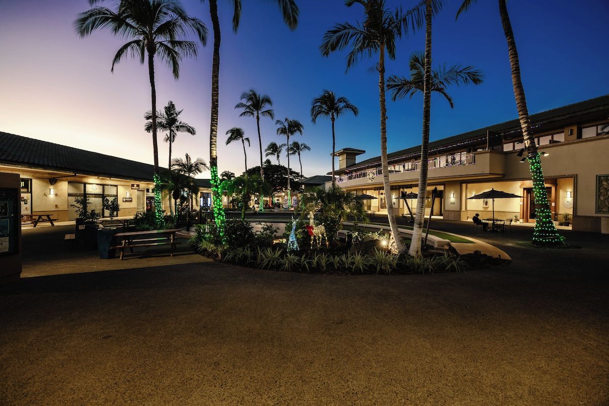A hotel courtyard with palm trees and a fountain, featuring outdoor seating and a covered area.