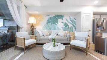 A modern living room with a sofa, two armchairs, a coffee table, and a kitchen area with a refrigerator.