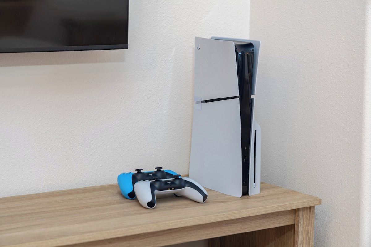Eine Spielkonsole und ein Controller auf einem Holzregal vor einer Wand.