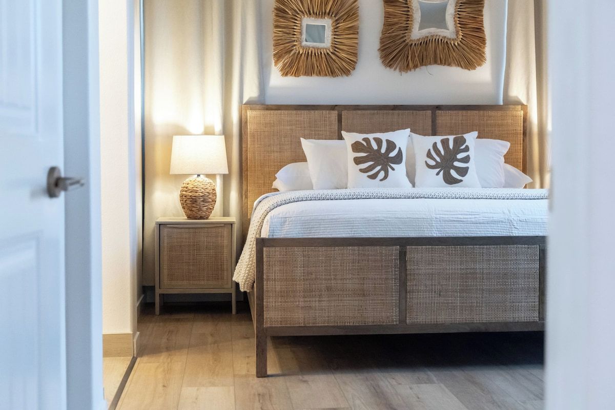 A bedroom with a wooden bed, white bedding, a nightstand with a lamp, and wall decor.