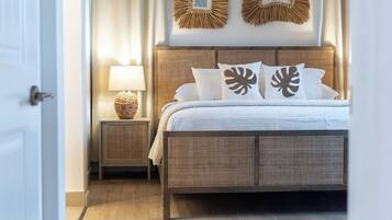 A bedroom with a wooden bed, white bedding, a nightstand with a lamp, and wall decor.
