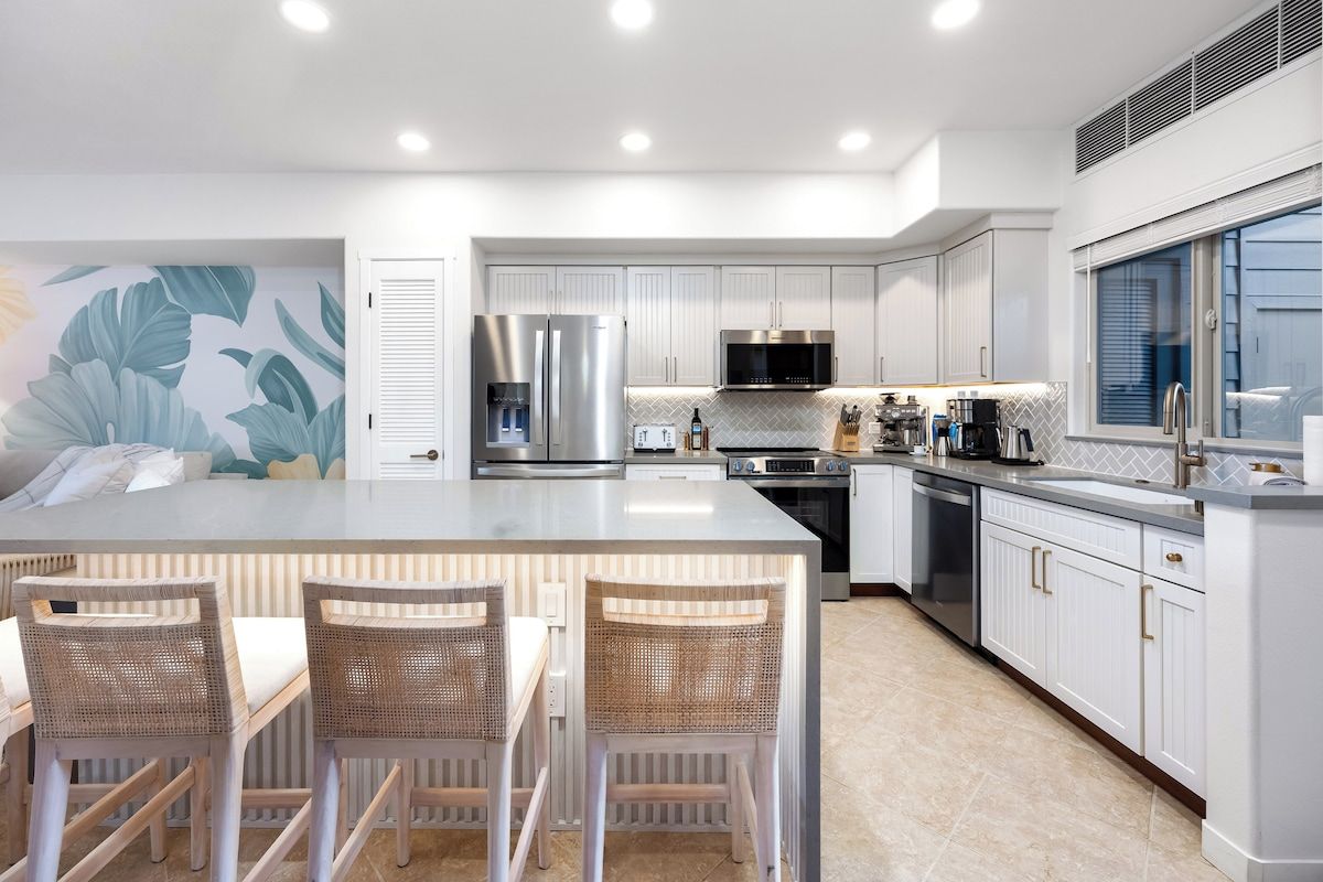 Una cocina moderna con muebles blancos, electrodomésticos de acero inoxidable y una isla grande con taburetes de bar.