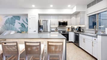 Una cocina moderna con muebles blancos, electrodomésticos de acero inoxidable y una isla grande con taburetes de bar.