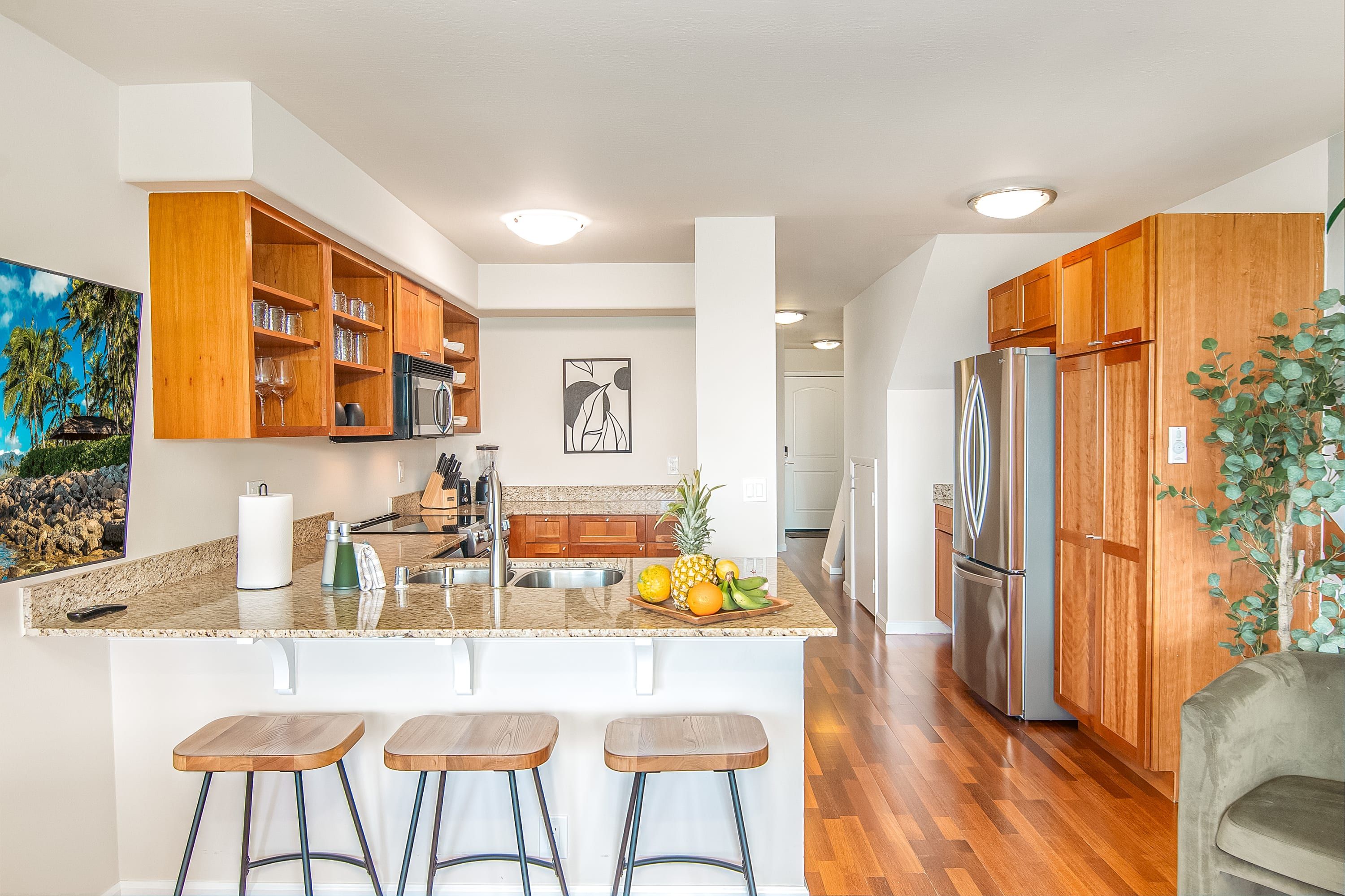 Una cocina moderna con armarios de madera, un refrigerador de acero inoxidable y una isla central con taburetes de bar.