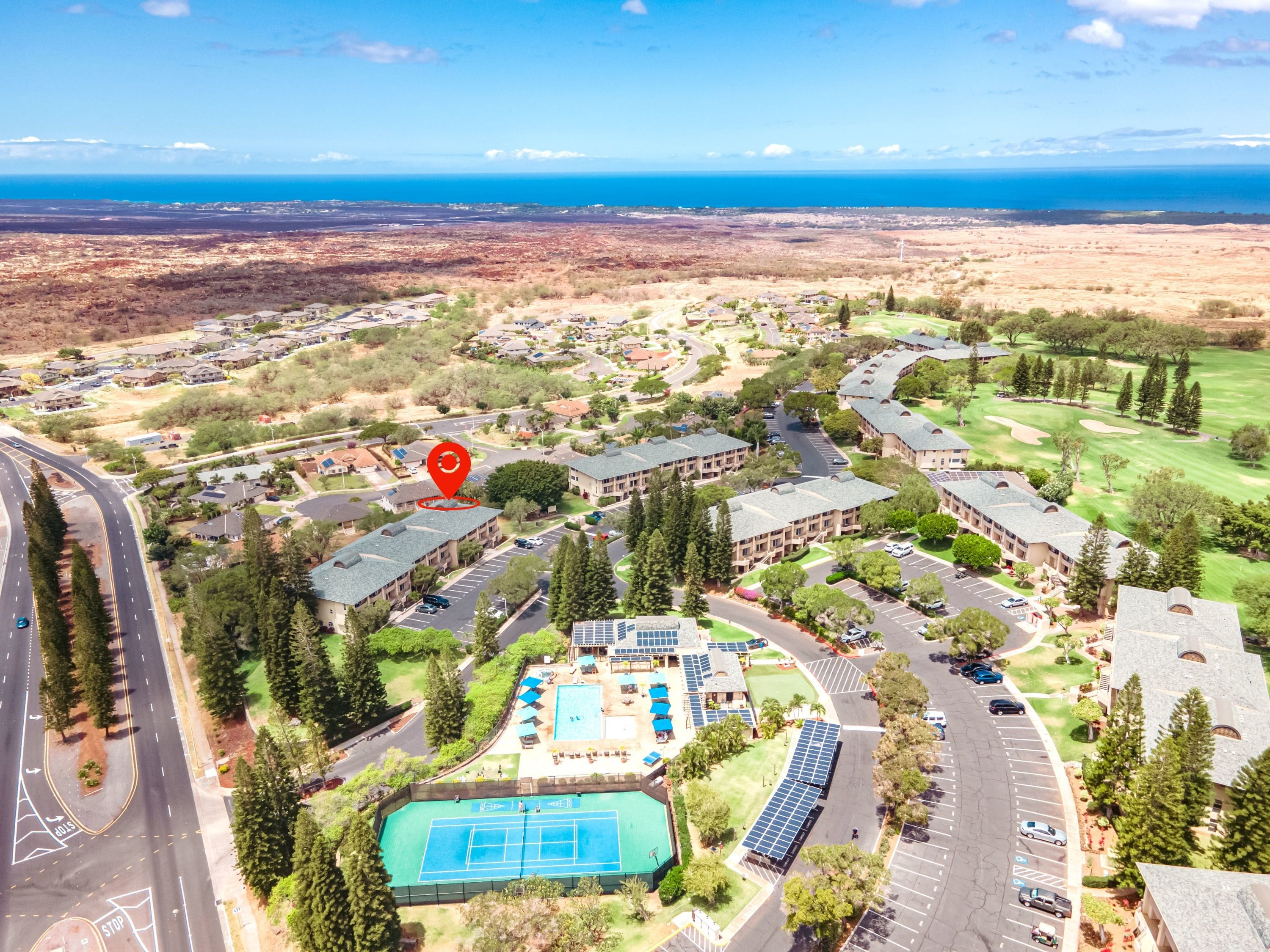 A residential area with a tennis court, parking, and a view of the ocean.