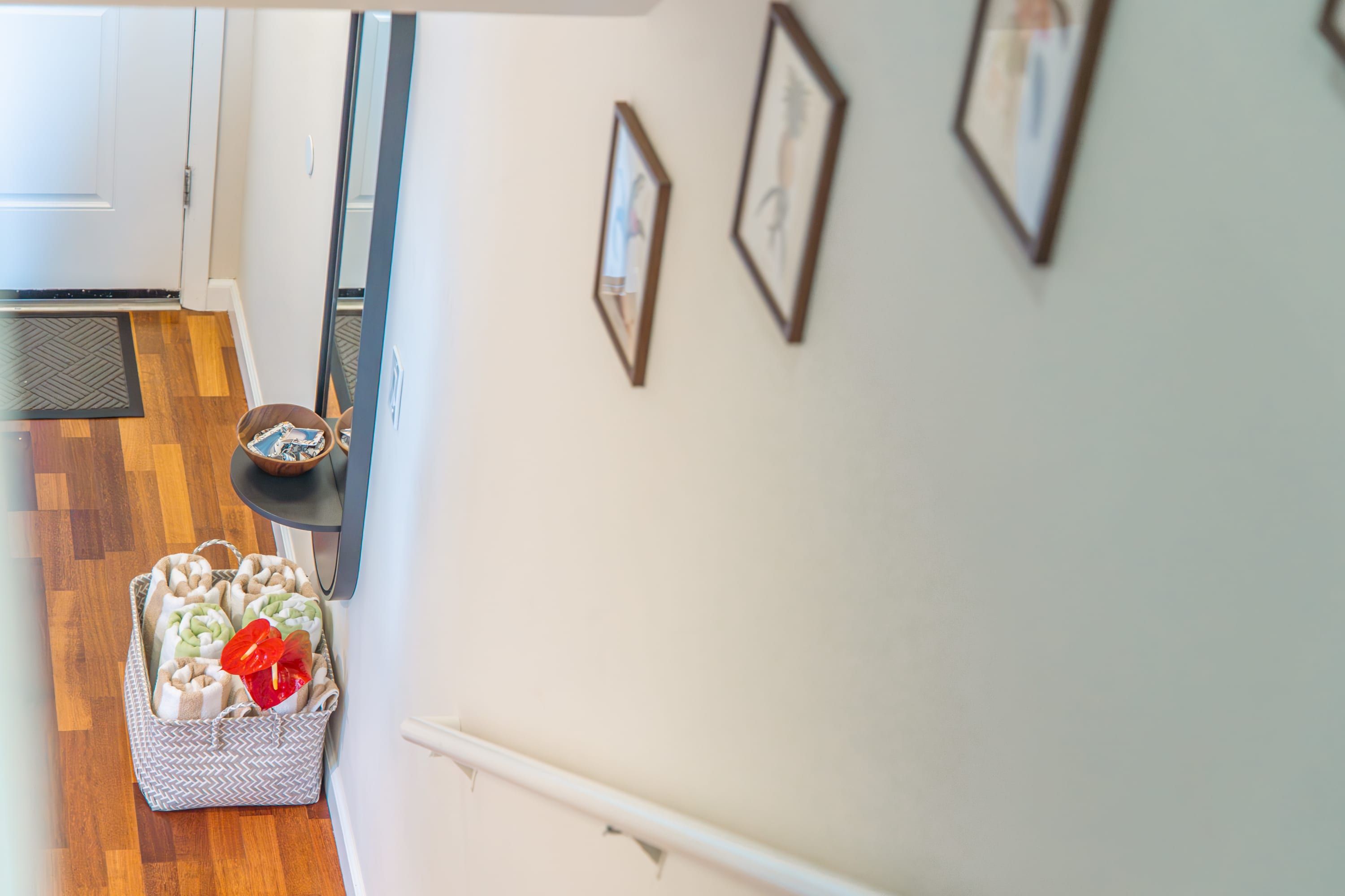 A hallway with a wooden floor, a white door, a small table with a bowl, and a pet bed with a red flower.
