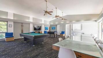 A modern indoor space with a pool table, a long dining table, and a conference table.