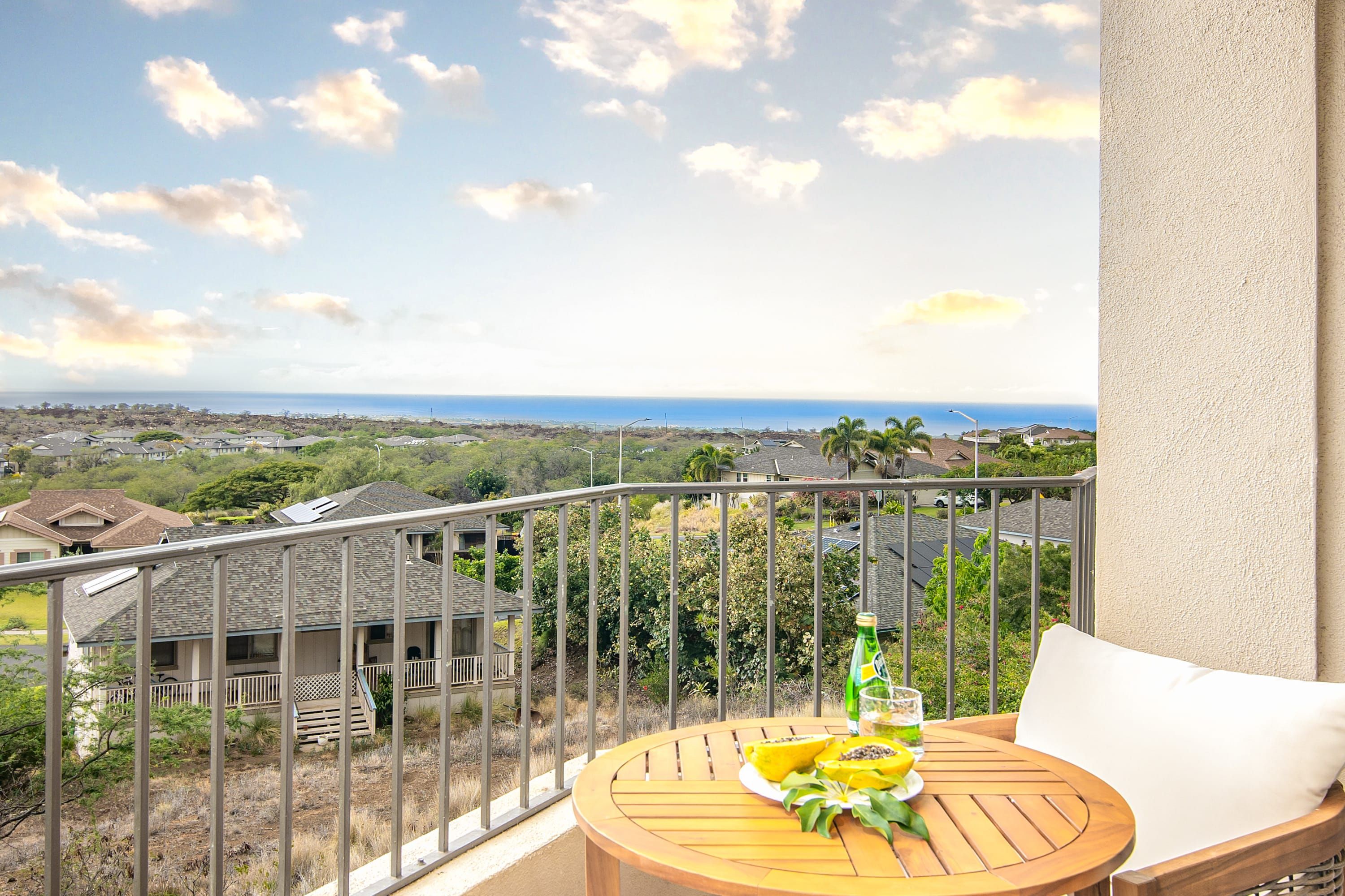 Varanda com vista para o oceano e uma mesa com garrafa e frutas.