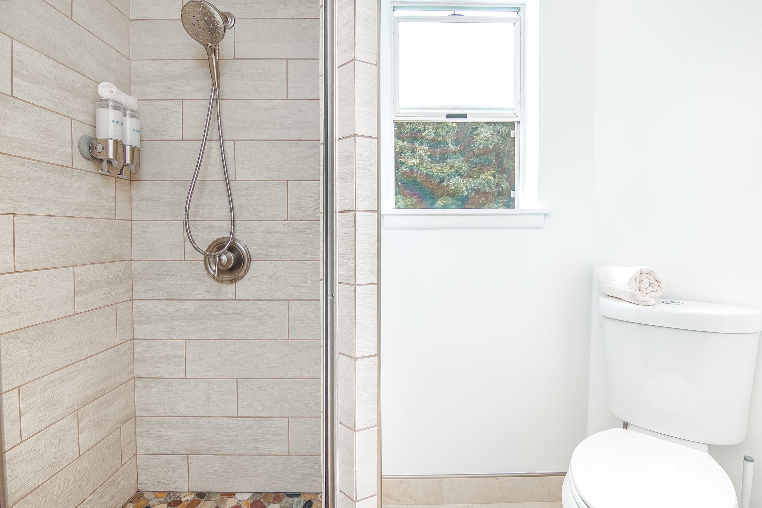 Une salle de bain avec douche, toilettes et une fenêtre donnant sur un espace verdoyant.