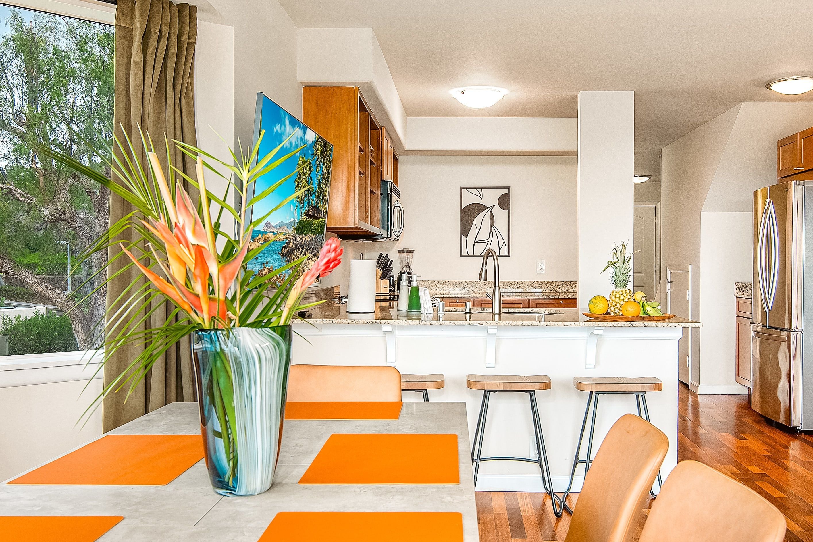 Una cocina moderna con una isla central, taburetes de bar y un amplio ventanal con cortinas.