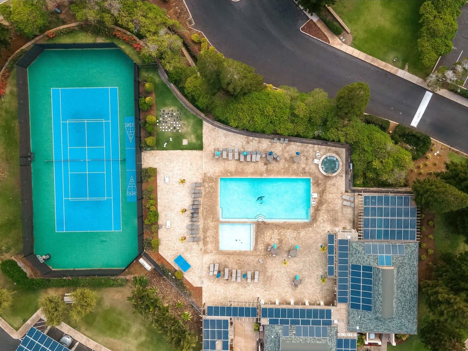 An aerial view of a property with a tennis court, a swimming pool, and solar panels.