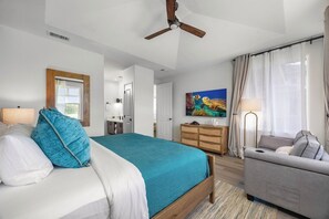 A bedroom with a bed, a desk, a chair, a ceiling fan, and a painting on the wall. - Treasure Retreat 3 bed Villa, Kings, Stylish Remodel (Waikoloa Village)